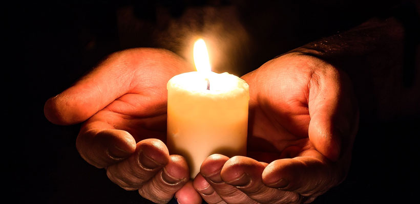 Lit candle held in hands.